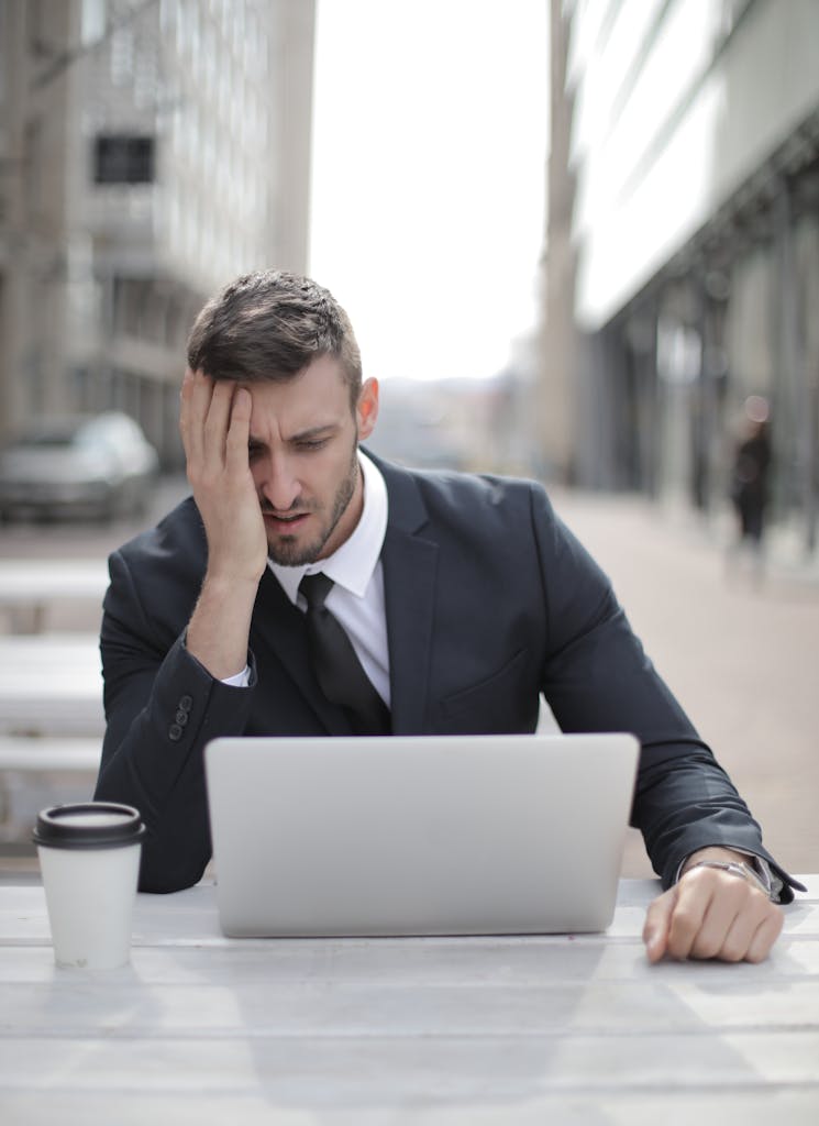 A businessman in a suit looking stressed while using a laptop outdoors.
