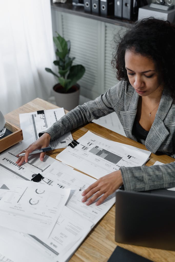 Professional woman reviewing documents and charts at a desk in a modern office.